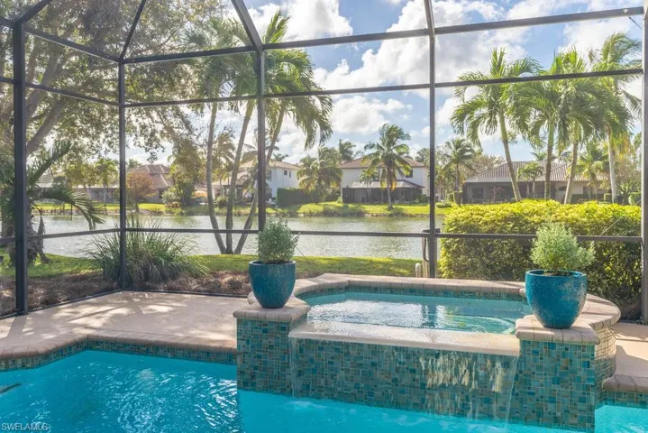 View of pool with glass enclosure, a water view, an in ground hot tub, and a patio