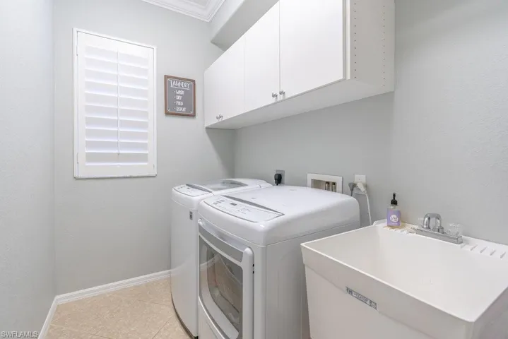 Laundry area featuring ornamental molding, sink, light tile patterned floors, washer and clothes dryer, and cabinets