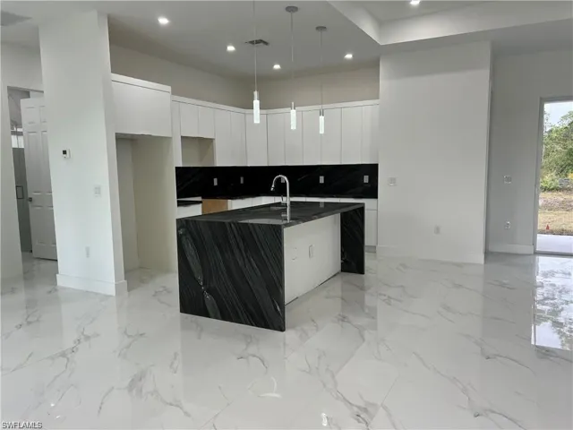 Kitchen with white cabinetry, light tile patterned floors, hanging light fixtures, decorative backsplash, and a center island with sink