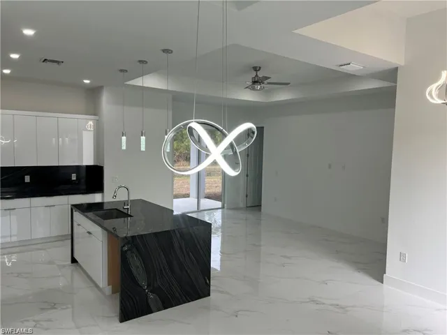Kitchen with dark stone counters, sink, decorative light fixtures, white cabinetry, and ceiling fan