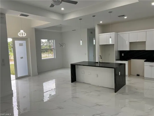 Kitchen featuring white cabinetry, ceiling fan, pendant lighting, light tile patterned floors, and a kitchen island with sink
