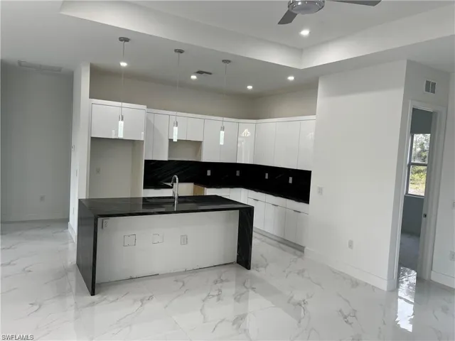 Kitchen with light tile patterned flooring, ceiling fan, white cabinets, and a center island with sink