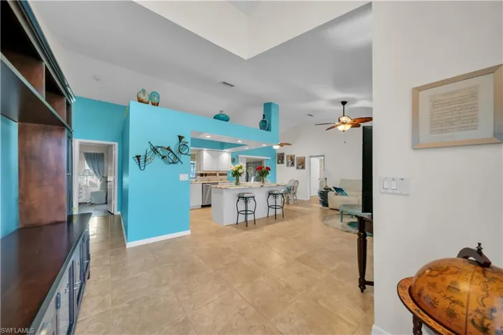 Kitchen with a breakfast bar area, lofted ceiling, a ceiling fan, white cabinets, and light stone counters