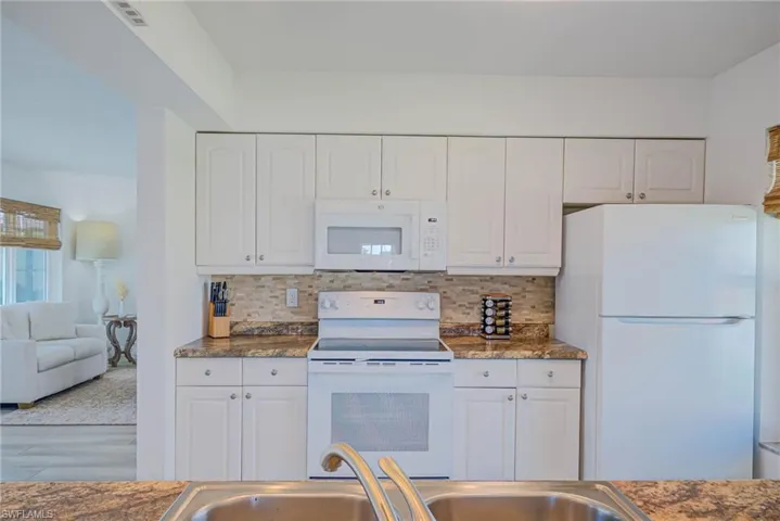 Kitchen featuring white cabinetry, visible vents, tasteful backsplash, and white appliances