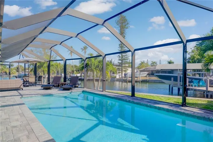 Outdoor pool featuring a dock, a water view, glass enclosure, and a patio