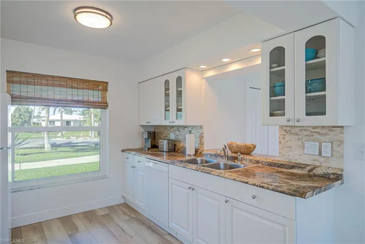 Kitchen featuring white cabinets, dishwasher, glass insert cabinets, a sink, and light wood-style floors