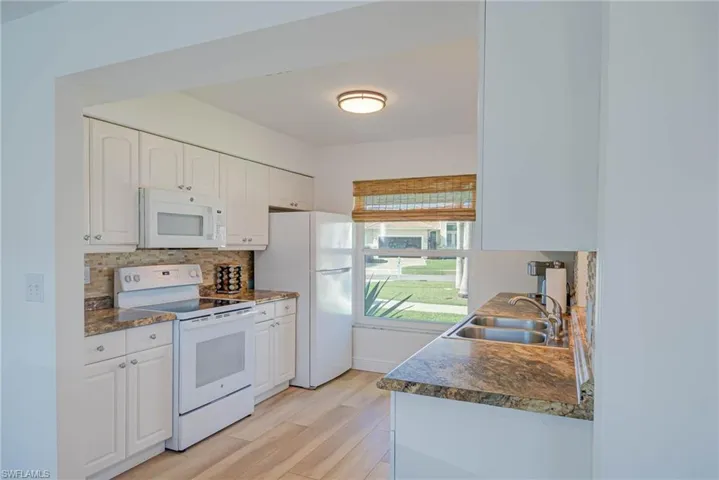 Kitchen with decorative backsplash, a sink, dark countertops, and white appliances