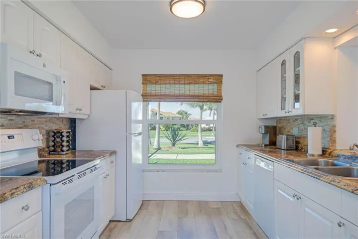 Kitchen featuring white cabinets, light wood-style flooring, white appliances, glass insert cabinets, and a sink