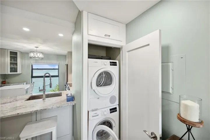 Washroom with stacked washing maching and dryer, sink, and an inviting chandelier