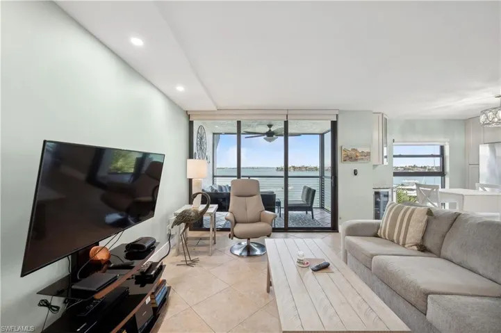 Living room featuring light tile floors, a water view, and ceiling fan with notable chandelier