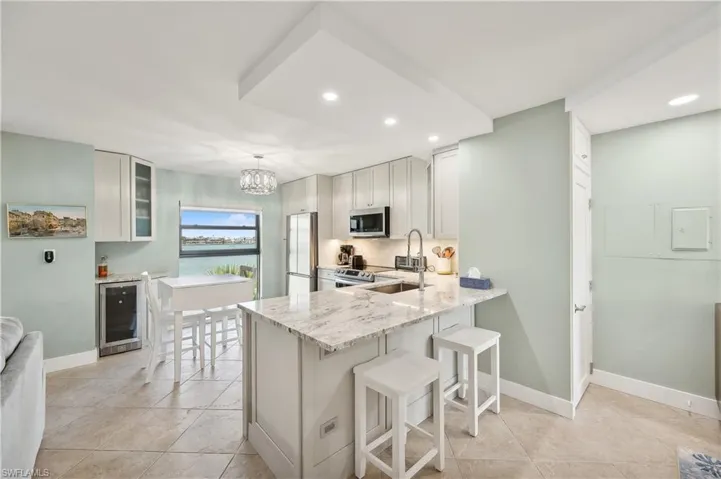 Kitchen featuring stainless steel appliances, wine cooler, pendant lighting, light tile flooring, and a kitchen bar