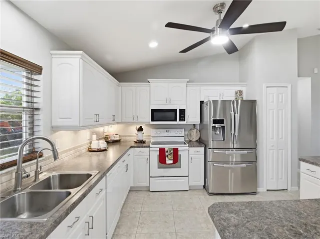 Kitchen with white appliances, white cabinets, recessed lighting, vaulted ceiling, and light tile patterned flooring