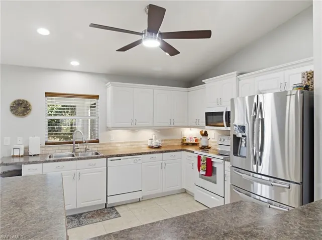 Kitchen with white appliances, white cabinetry, a ceiling fan, light tile patterned floors, and vaulted ceiling