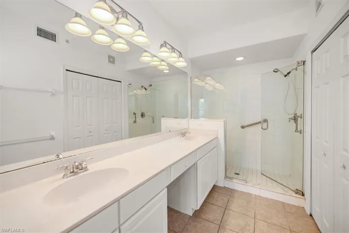 featuring a double vanity with integrated sinks, a glass-enclosed shower with a tiled surround, a large wall-mounted mirror, and tile flooring