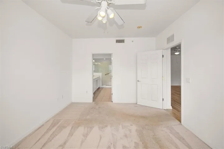 Carpeted room featuring a ceiling fan with integrated lighting, a doorway to a bathroom with tile flooring, and a separate doorway to a room with wood-finish flooring