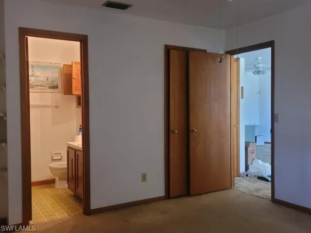 Unfurnished bedroom with ensuite bathroom and light carpet