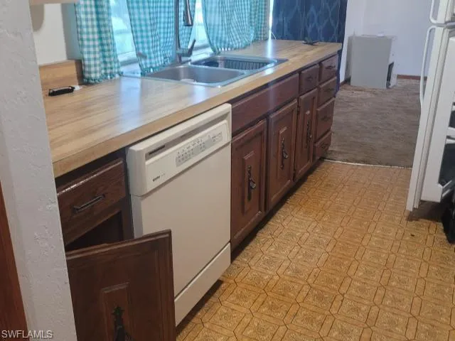 Kitchen with sink, light carpet, white dishwasher, and dark brown cabinets