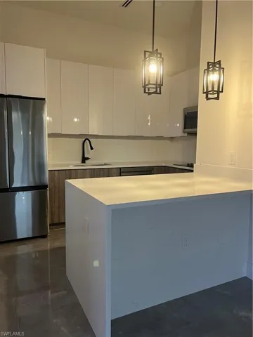 Kitchen featuring a peninsula, white cabinetry, refrigerator, modern cabinets, and hanging light fixtures