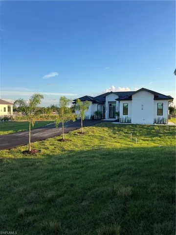 Rear view of property featuring a yard, driveway, and stucco siding