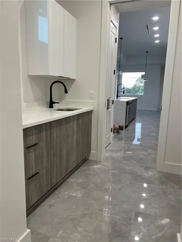 Bar featuring modern cabinets, light marble finish floors, white cabinetry, hanging light fixtures, and light stone countertops