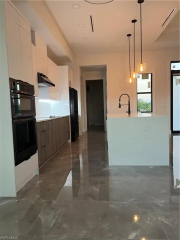 Kitchen featuring modern cabinets, hanging light fixtures, white cabinetry, double oven, and stainless steel fridge