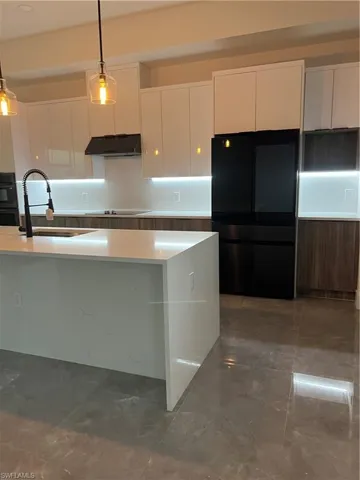 Kitchen featuring modern cabinets, white cabinetry, refrigerator, pendant lighting, and exhaust hood