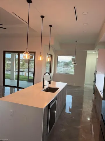 Kitchen with pendant lighting, light stone countertops, a center island with sink, dark marble finish flooring, and dishwasher