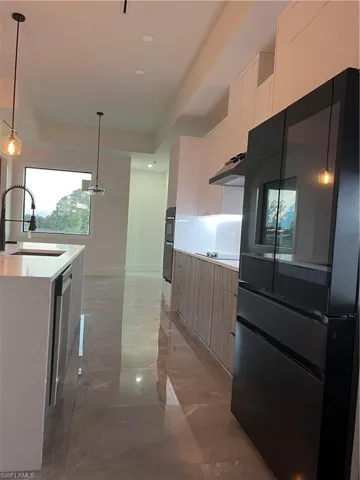 Kitchen with pendant lighting, white cabinets, black fridge, modern cabinets, and light marble finish floors