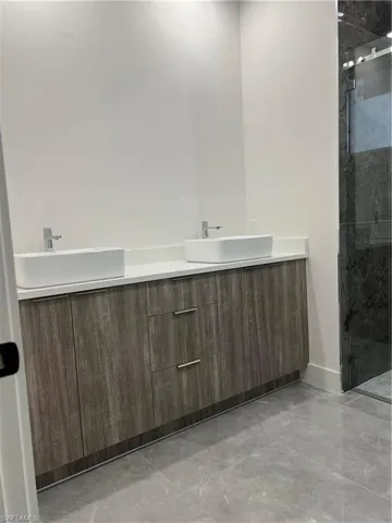 Bathroom with double vanity, a marble finish shower, and light marble finish flooring