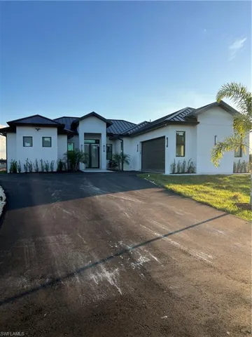 View of front of home with a standing seam roof, concrete driveway, a metal roof, and stucco siding