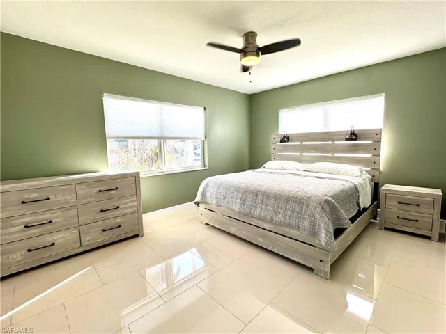 Tiled bedroom featuring multiple windows and ceiling fan