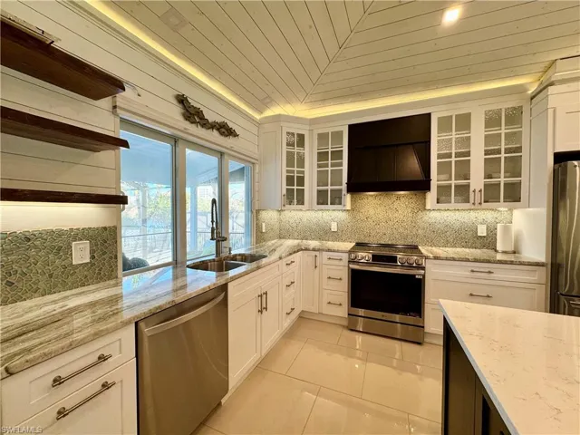 Kitchen with white cabinets, custom exhaust hood, sink, and appliances with stainless steel finishes