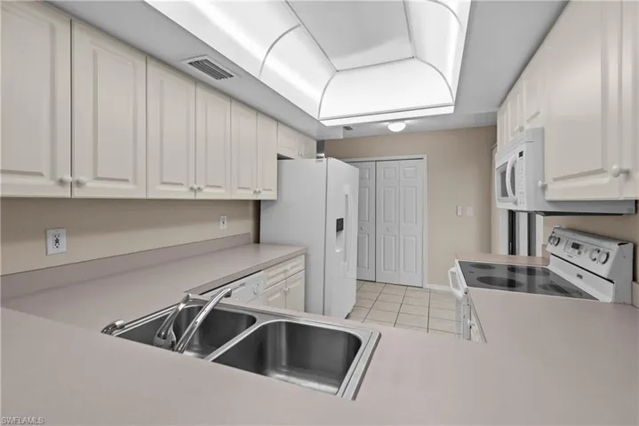 Kitchen featuring sink, white cabinetry, white appliances, and light tile patterned floors