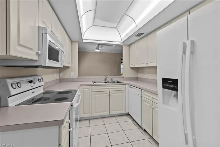 Kitchen with ceiling fan, white cabinets, white appliances, sink, and light tile patterned floors