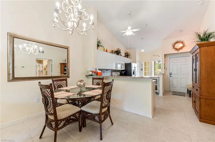 Dining room with high vaulted ceiling, light tile patterned floors, ceiling fan with notable chandelier, and baseboards