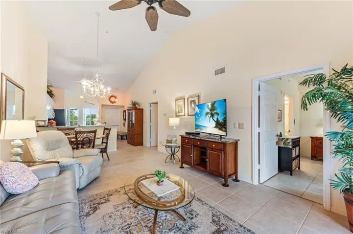 Living room featuring visible vents, high vaulted ceiling, light tile patterned floors, and ceiling fan with notable chandelier
