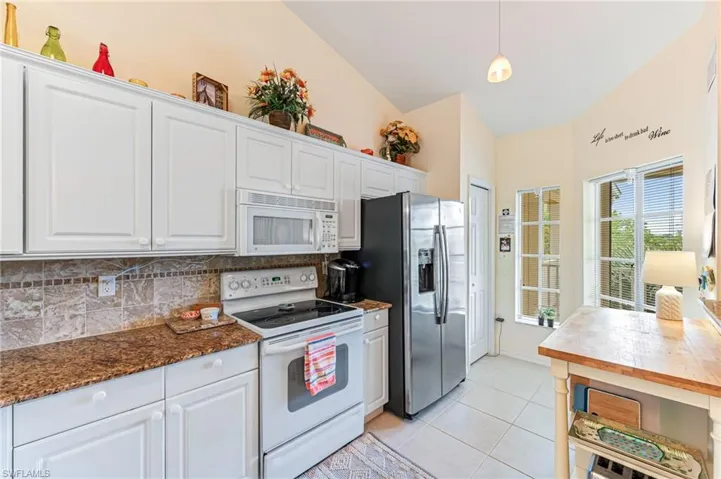 Kitchen with white appliances, light tile patterned floors, white cabinetry, lofted ceiling, and decorative backsplash