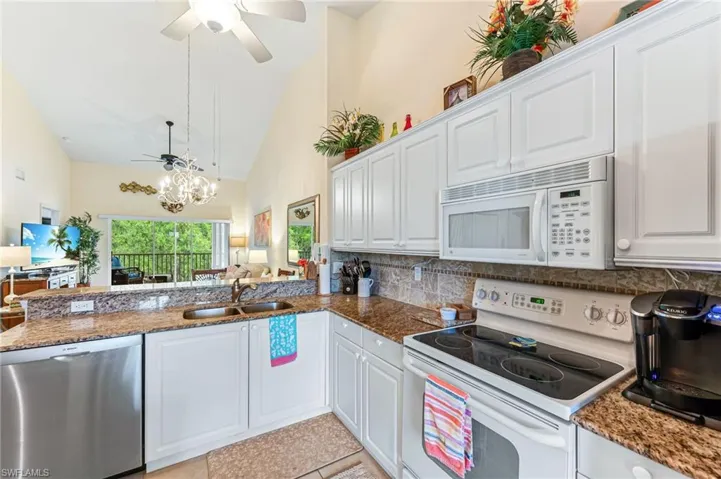 Kitchen with white cabinetry, ceiling fan with notable chandelier, a sink, and white appliances