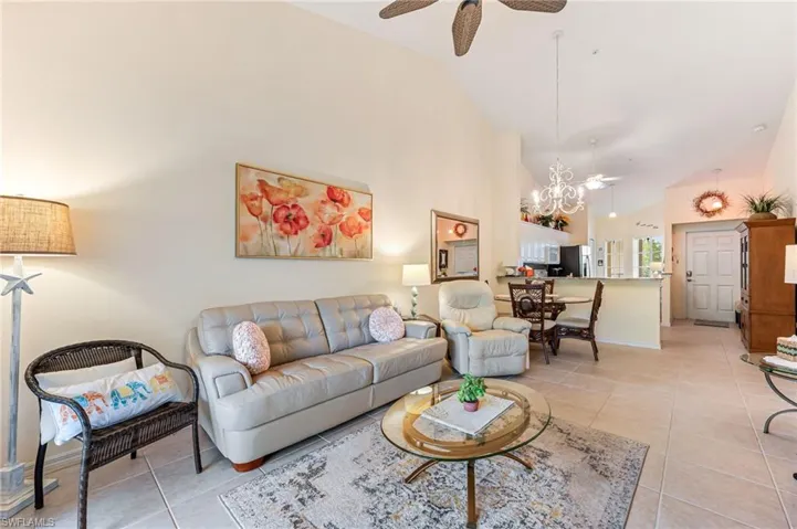 Living area with light tile patterned floors, baseboards, high vaulted ceiling, and ceiling fan with notable chandelier