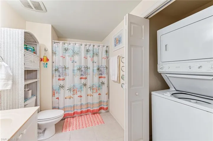 Bathroom with vanity, stacked washer and dryer, tile patterned flooring, toilet, and visible vents