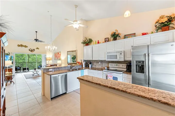 Kitchen with high vaulted ceiling, a peninsula, light tile patterned floors, stainless steel appliances, and ceiling fan with notable chandelier
