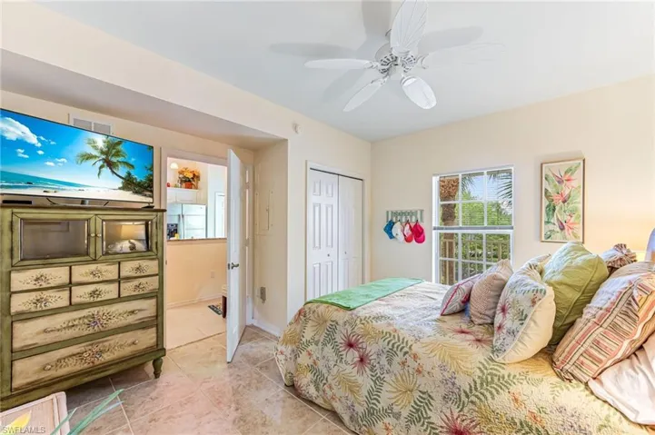 Bedroom with white refrigerator with ice dispenser, a closet, light tile patterned flooring, and ceiling fan