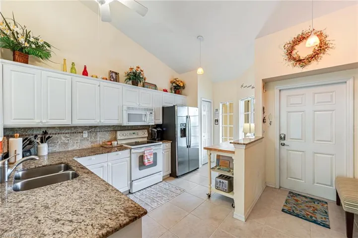 Kitchen with tasteful backsplash, white cabinets, a sink, white appliances, and light tile patterned flooring