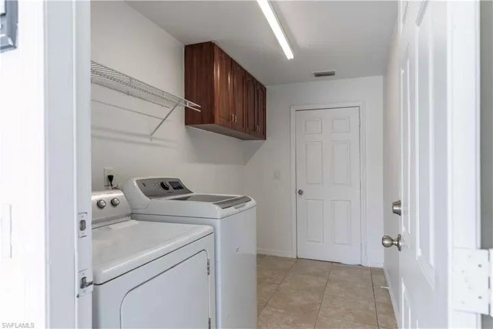 Laundry room with light tile patterned flooring, cabinets, and separate washer and dryer
