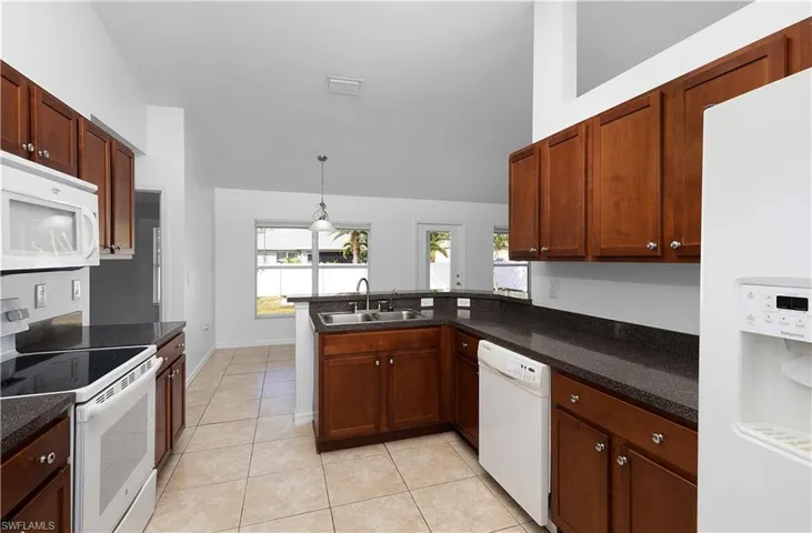 Kitchen with sink, kitchen peninsula, pendant lighting, white appliances, and light tile patterned floors