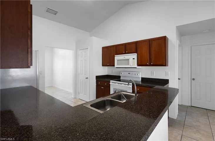 Kitchen with white appliances, high vaulted ceiling, sink, light tile patterned floors, and kitchen peninsula