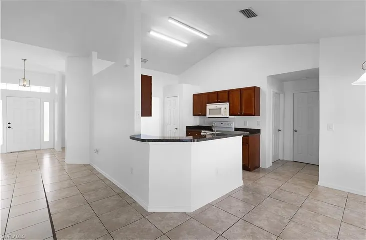 Kitchen with kitchen peninsula, white appliances, vaulted ceiling, pendant lighting, and light tile patterned floors