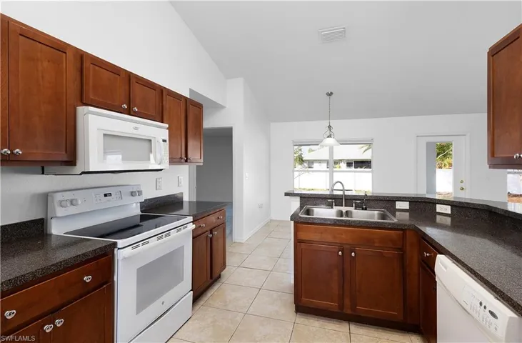 Kitchen featuring vaulted ceiling, plenty of natural light, sink, and white appliances