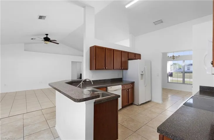 Kitchen with kitchen peninsula, white appliances, ceiling fan with notable chandelier, high vaulted ceiling, and light tile patterned flooring