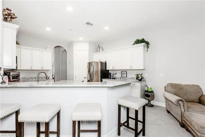 Kitchen with a kitchen bar, light stone countertops, white cabinetry, arched walkways, and a peninsula